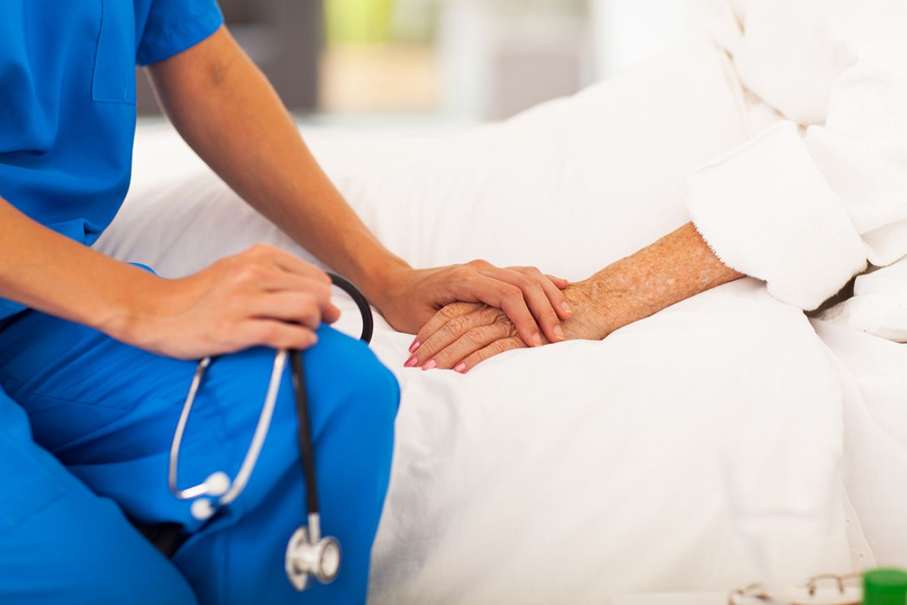 A shutterstock photo of a healthcare worker holding their client's hand.